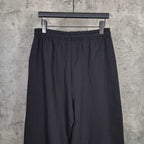 Balenciaga black pants with elastic waistband, draped fabric, front view on hanger