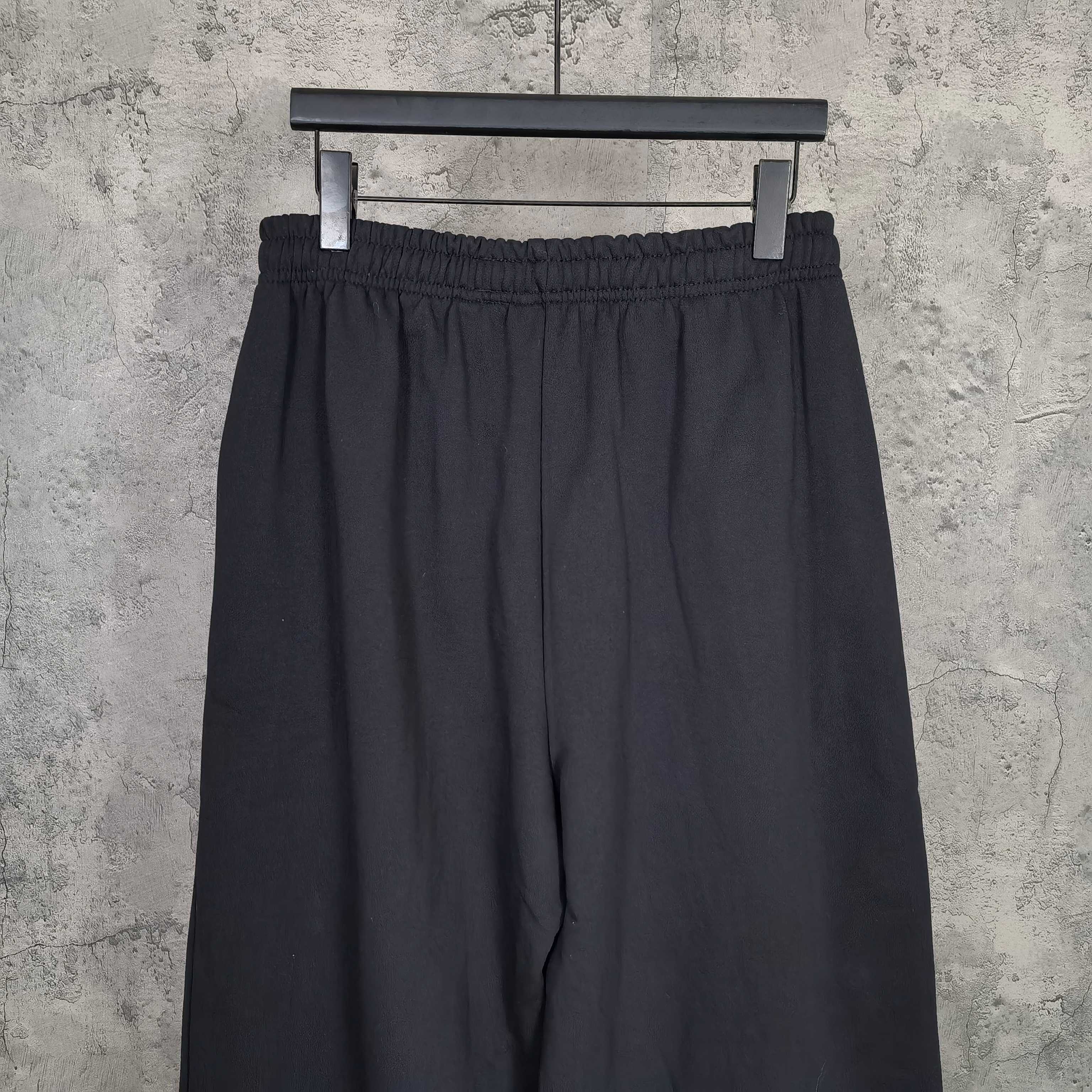 Balenciaga black pants with elastic waistband, draped fabric, front view on hanger
