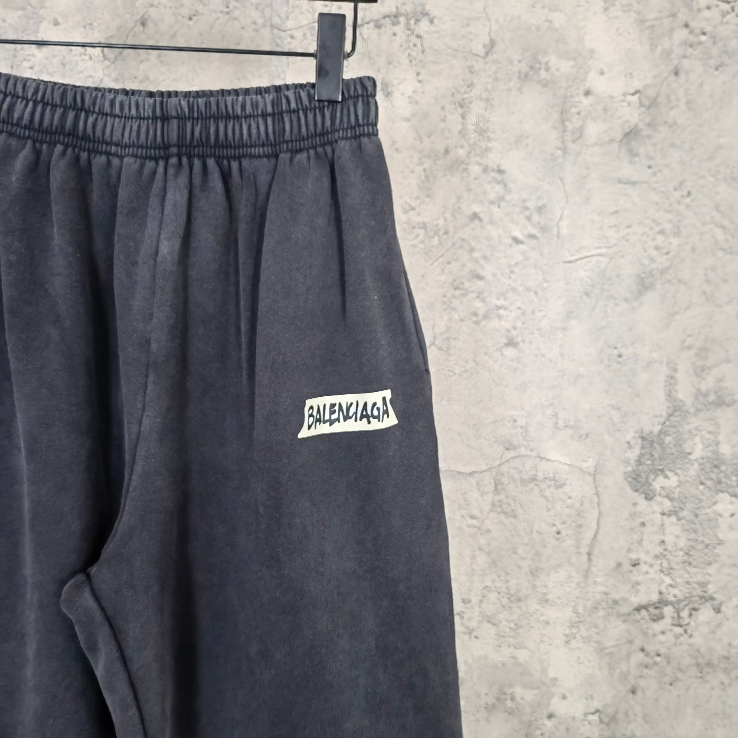 Dark sweatpants with elastic waistband and small BALENCIAGA logo patch on thigh.
