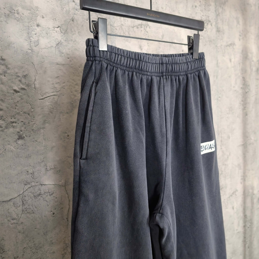 Dark sweatpants with elastic waistband and BALENCIAGA logo patch near hem.