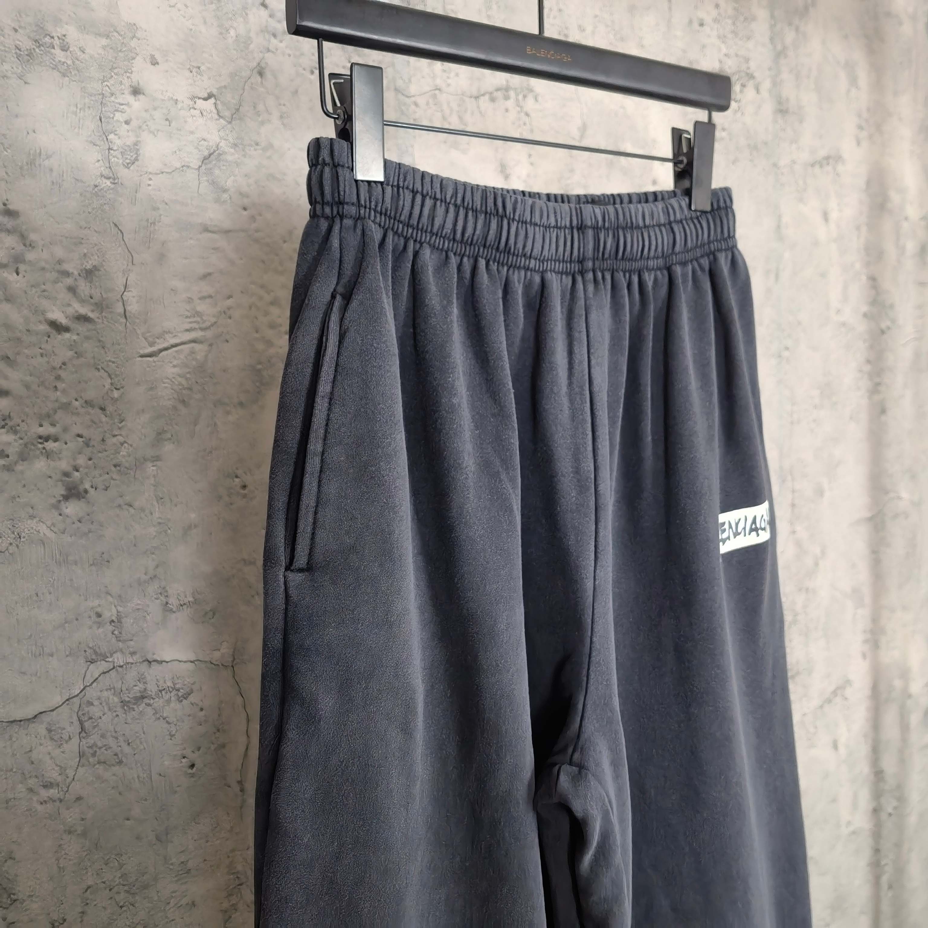 Dark sweatpants with elastic waistband and BALENCIAGA logo patch near hem.