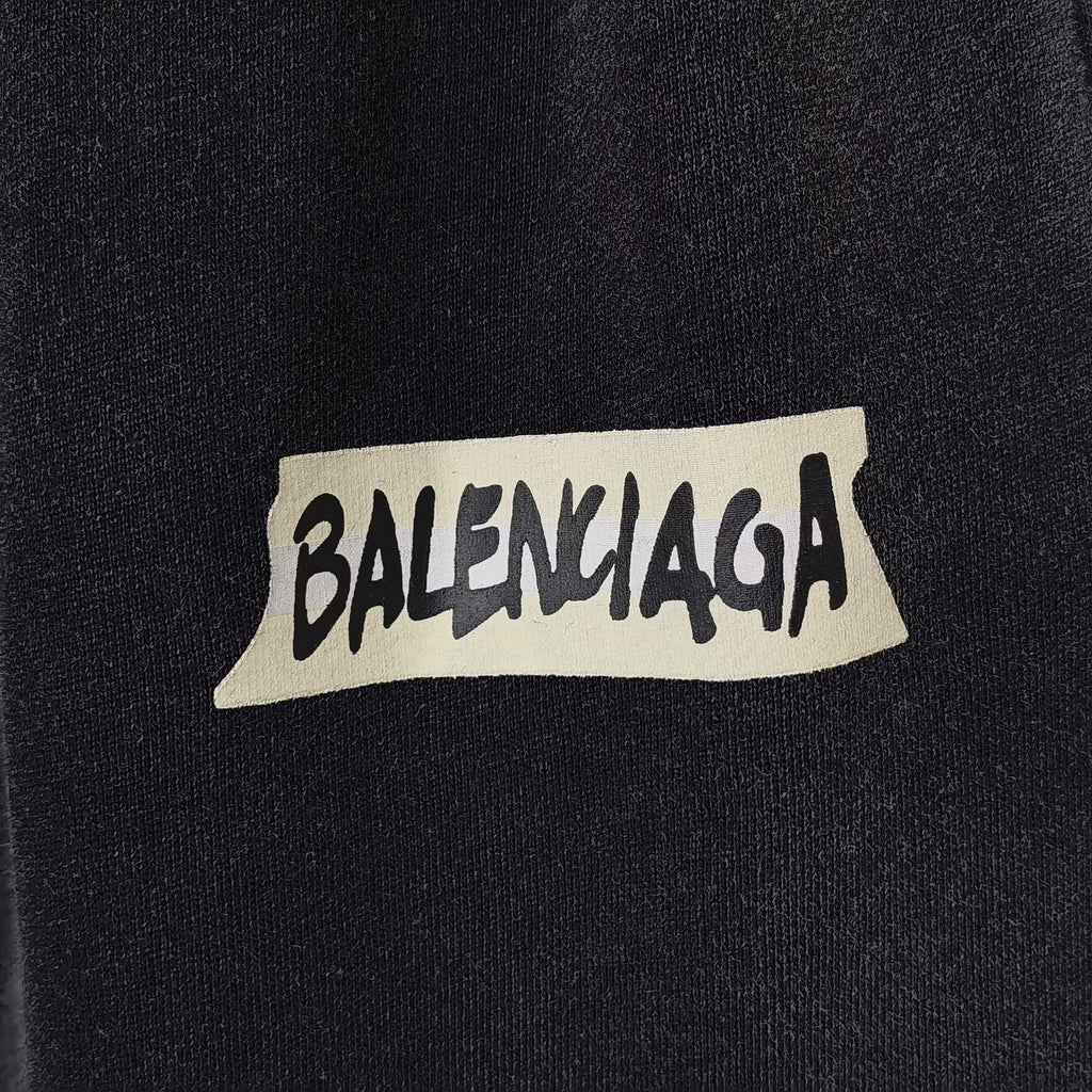 BALENCIAGA logo patch on dark fabric, white label with black lettering.