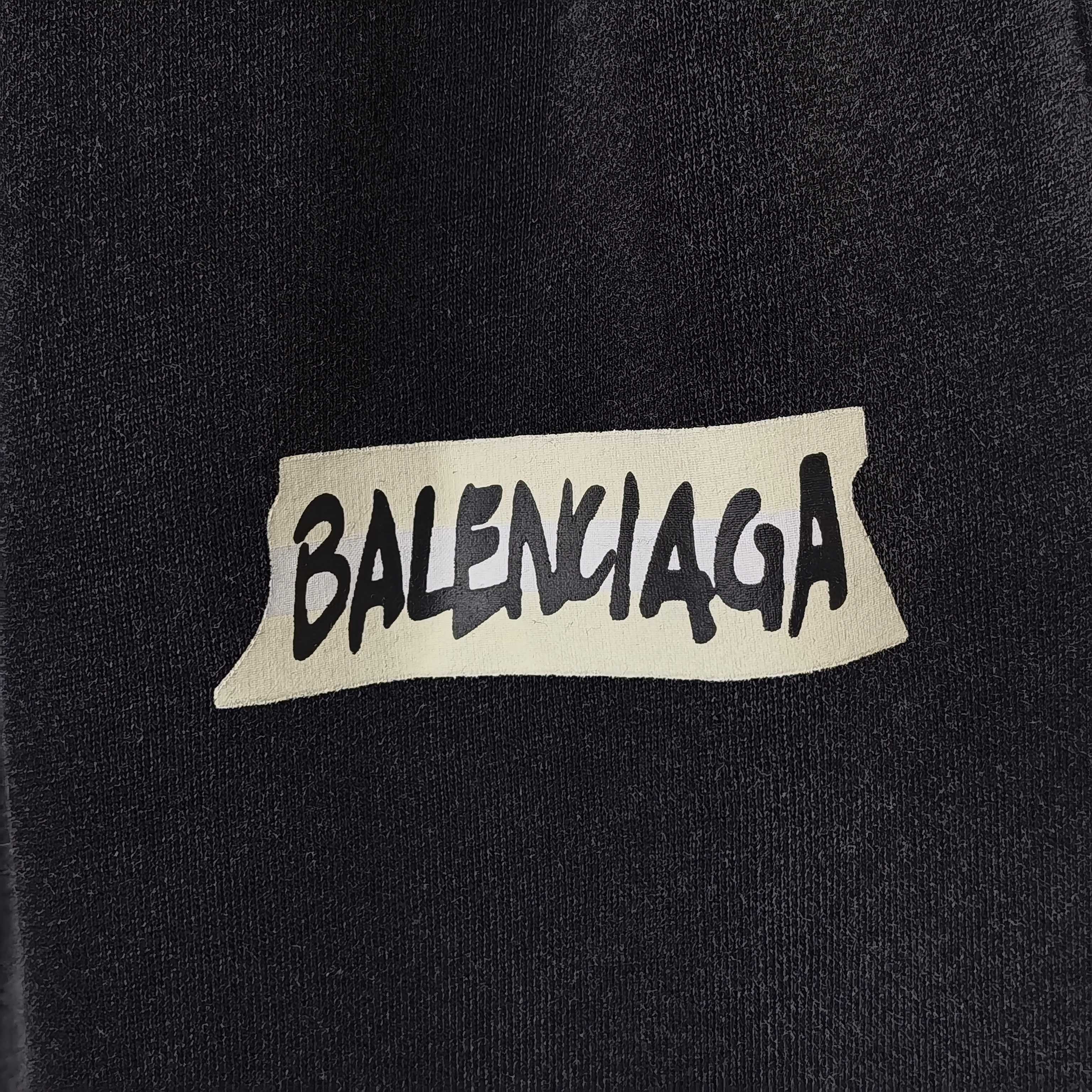 BALENCIAGA logo patch on dark fabric, white label with black lettering.
