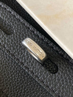 Louis Vuitton black leather handbag with metal logo plate on textured surface