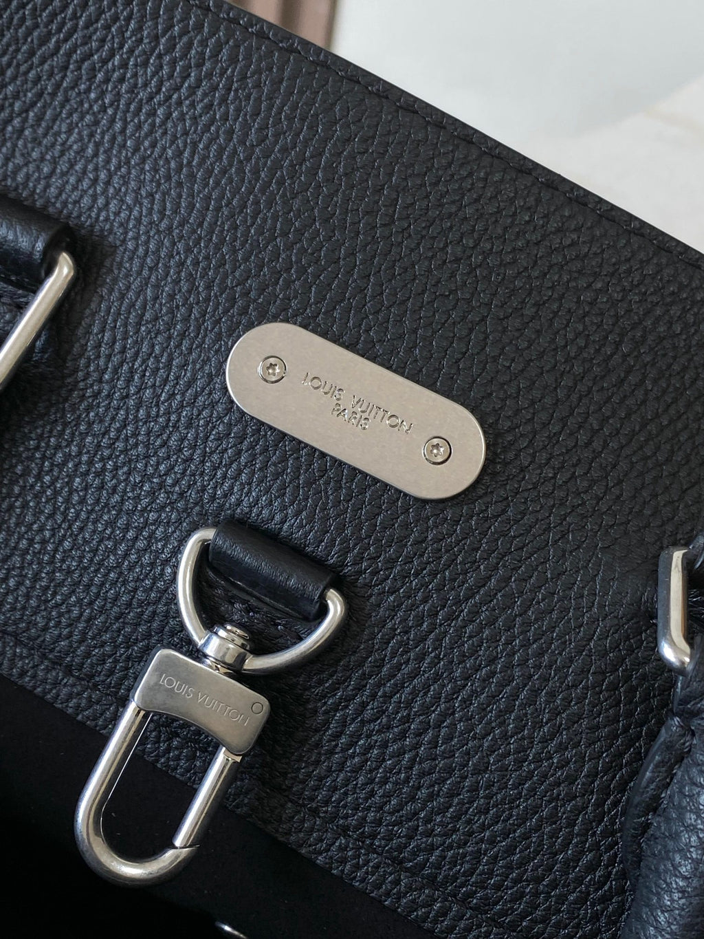 Louis Vuitton bag front with metal plaque and D-ring strap hardware, dark pebbled leather