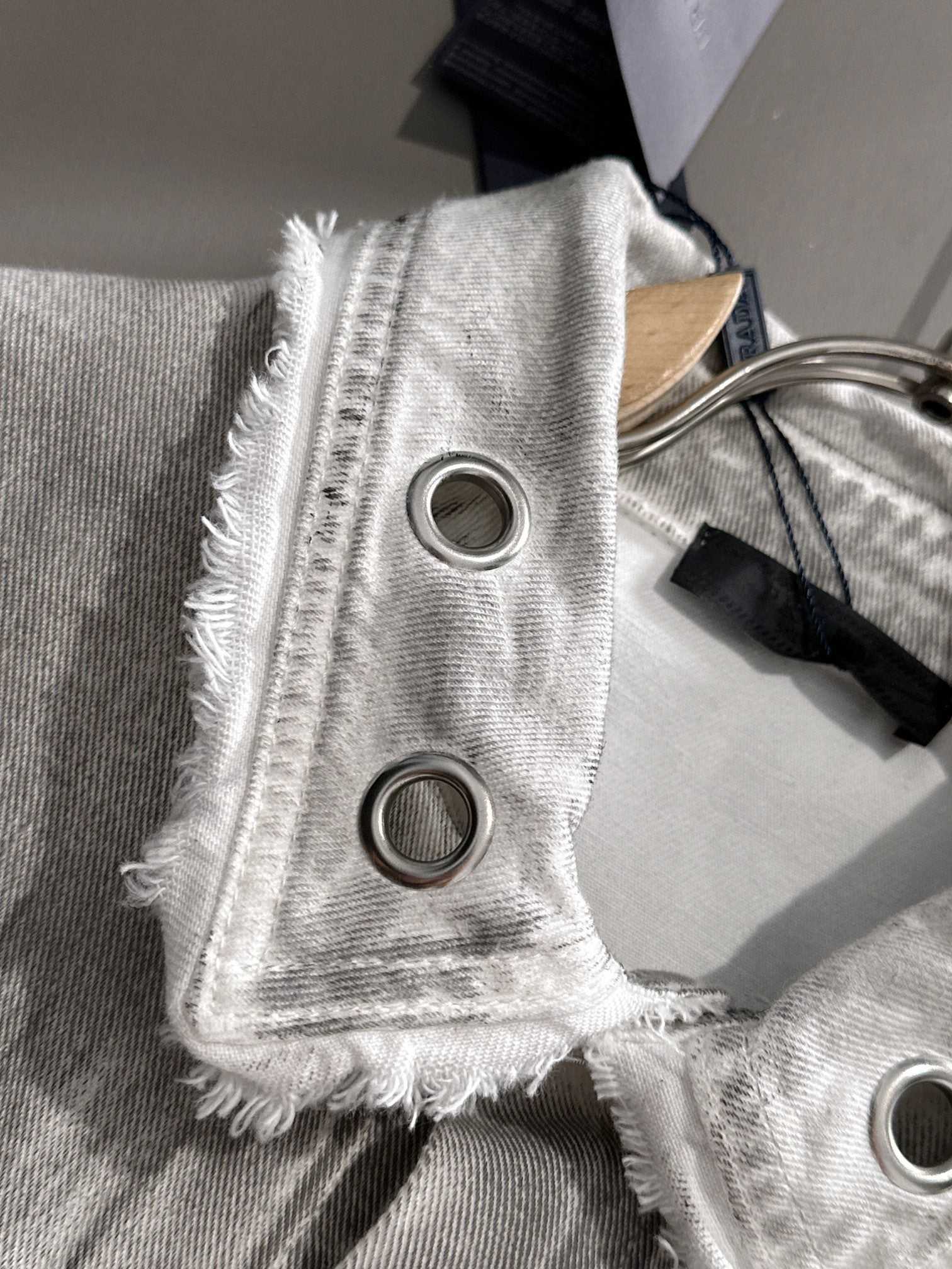 White denim strap detail with frayed edges and two round ring eyelets