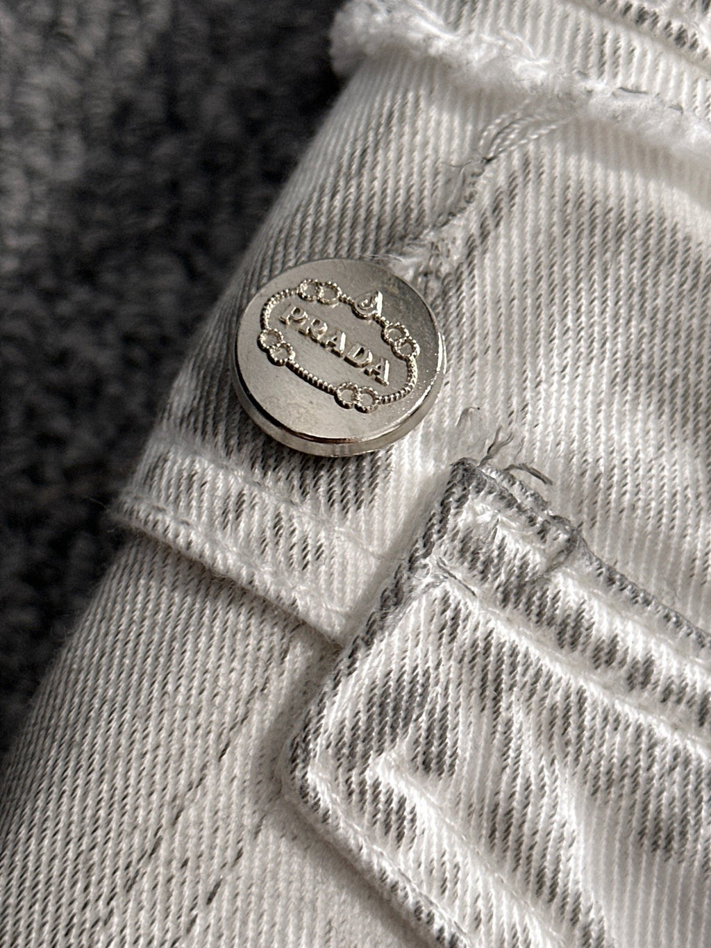 Light denim cuff close-up with round metal logo button and frayed stitching