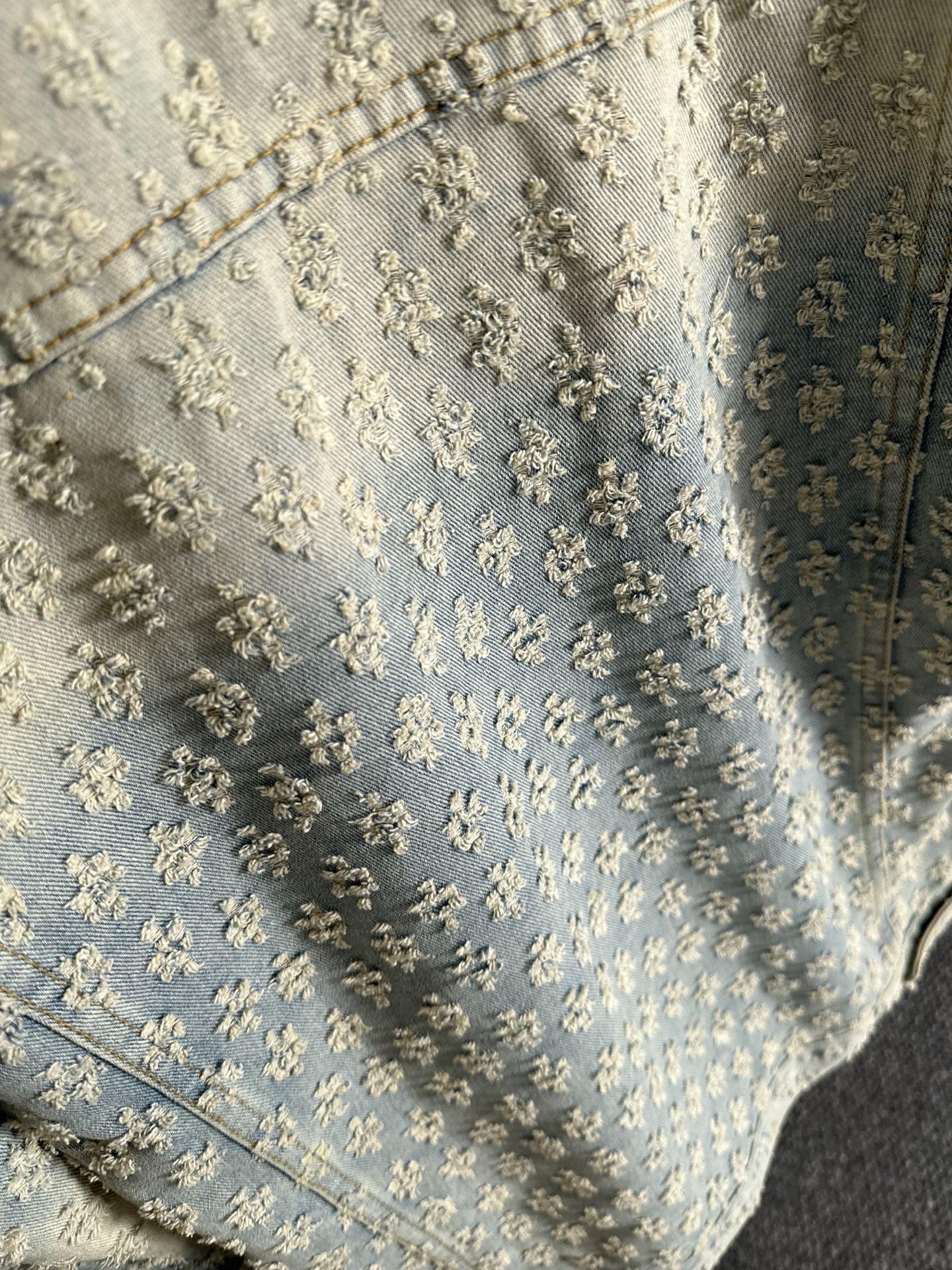 Light blue denim fabric with dense floral embroidery texture and stitched seams
