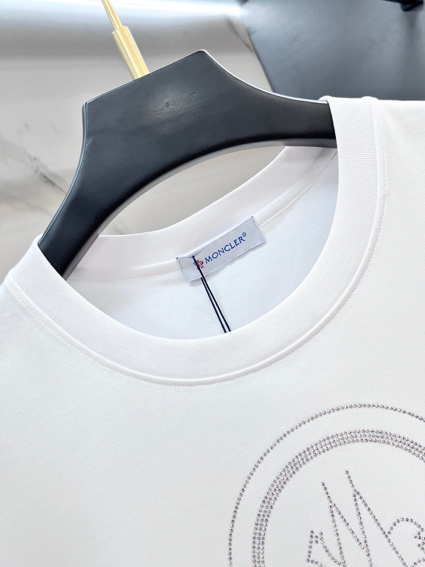 White Moncler T-shirt neckline with brand tag and rhinestone logo detail.