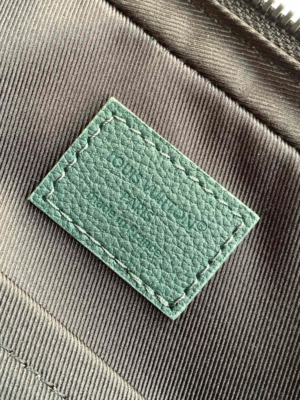Louis Vuitton teal leather bag tag or card holder on textured fabric