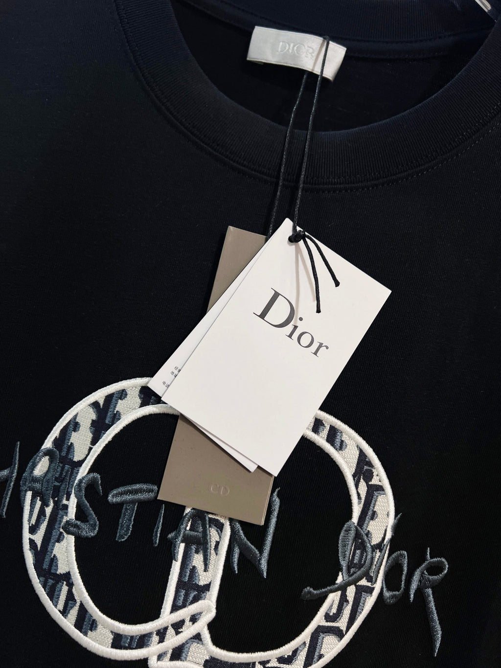 Black Dior T-shirt with hanging white tag at crew neckline