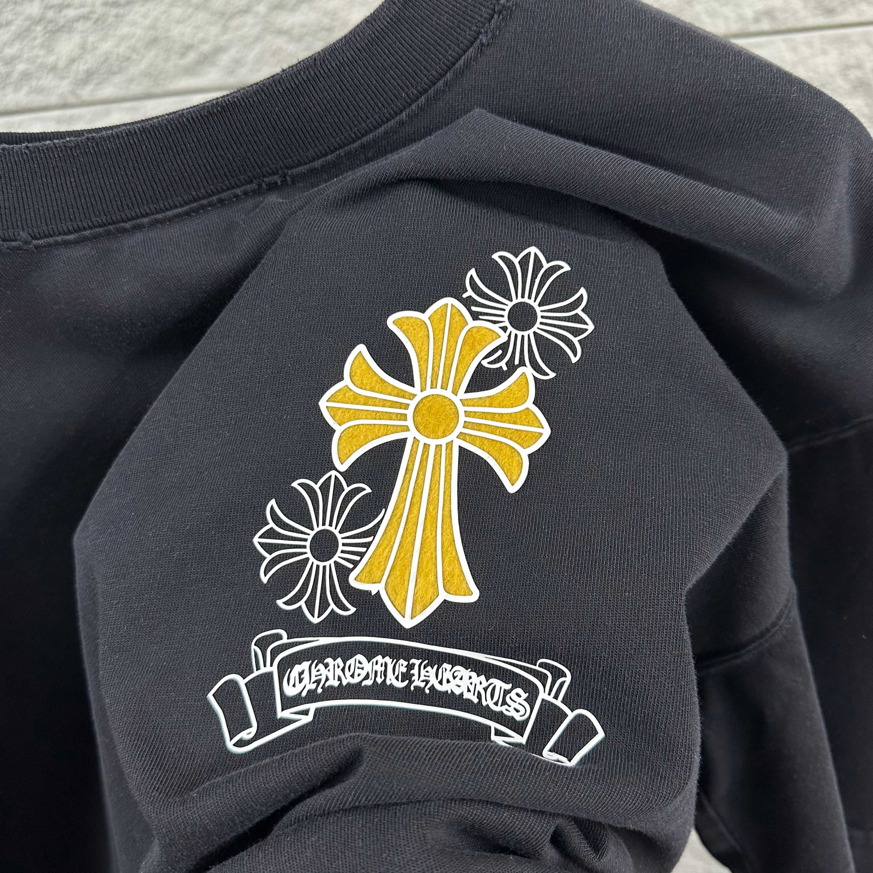 Dark T-shirt neckline and chest graphic: cross-flower with banner