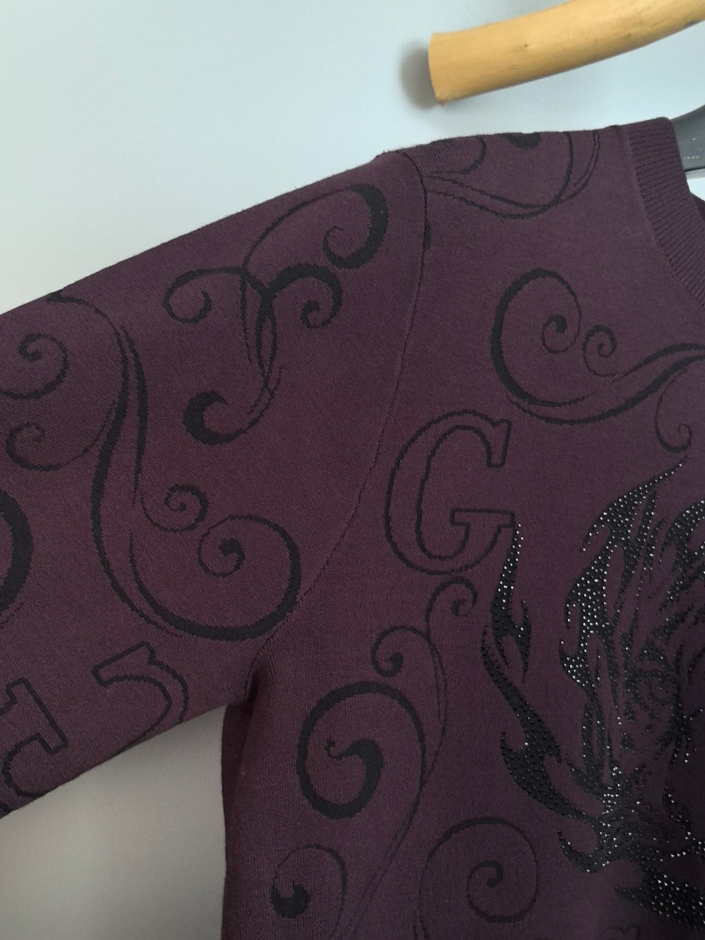 Long-sleeve sweater sleeve in dark plum with curled swirl pattern and black sequin detail