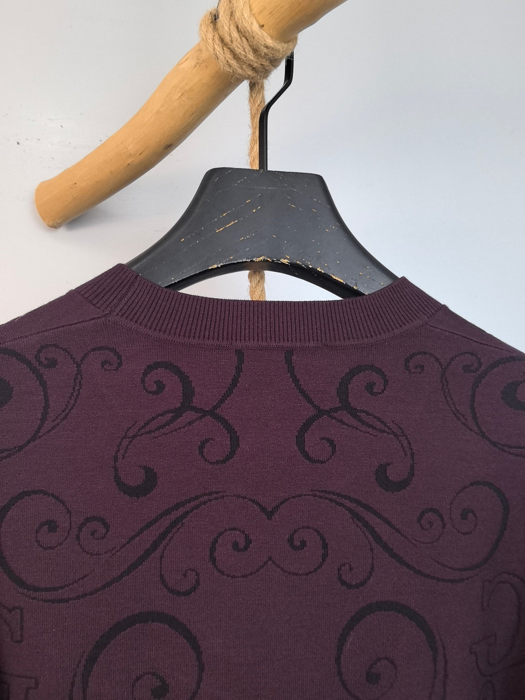 Dark plum crewneck sweater collar with repeating swirl pattern across the upper back