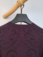 Dark plum crewneck sweater collar with repeating swirl pattern across the upper back