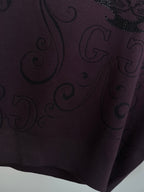 Dark plum sweater fabric close-up with woven swirl pattern and small sparkle accents