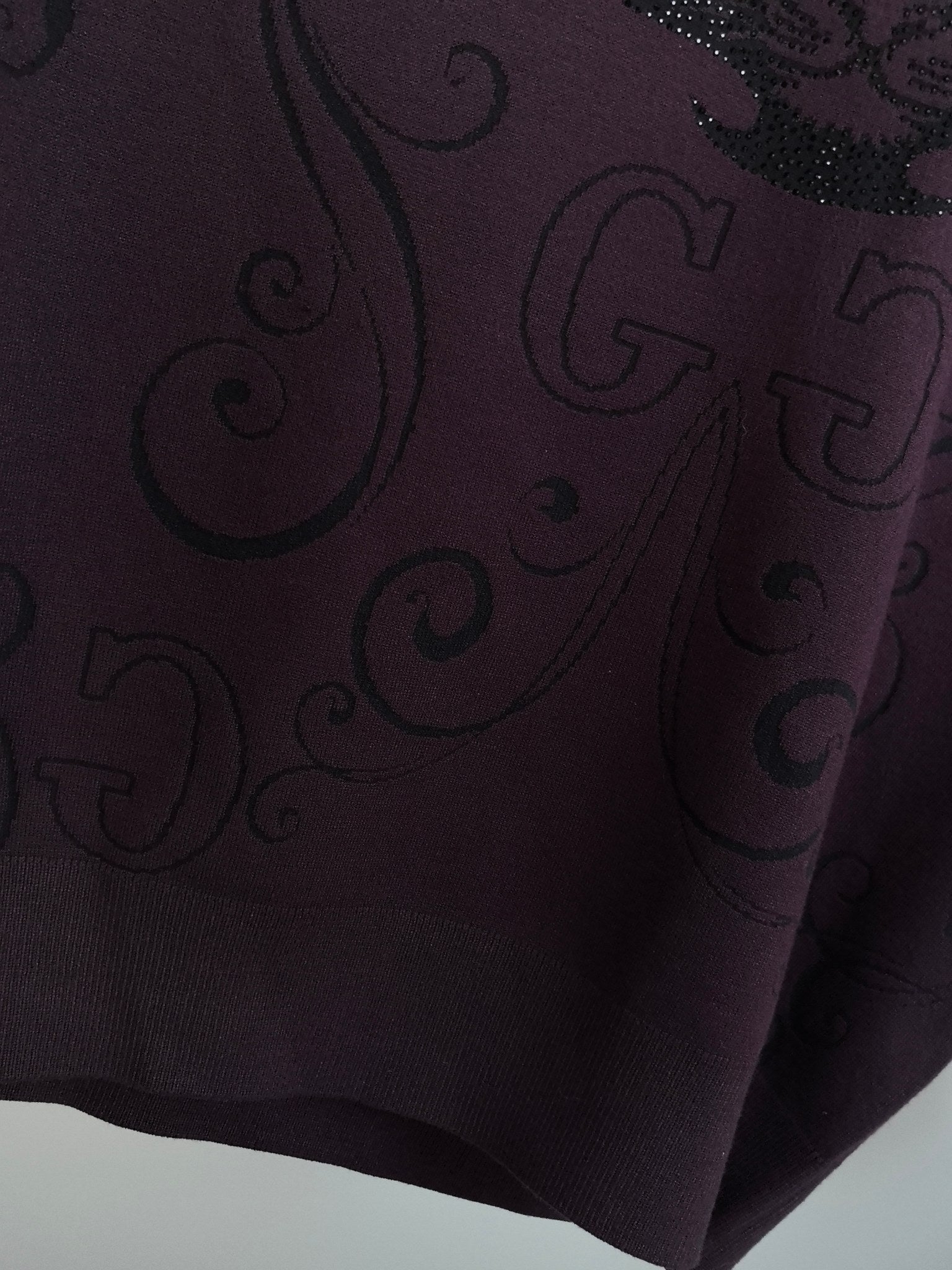 Dark plum sweater fabric close-up with woven swirl pattern and small sparkle accents