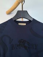 Burberry long-sleeve sweater close-up of crew neck and gold logo patch on collar.