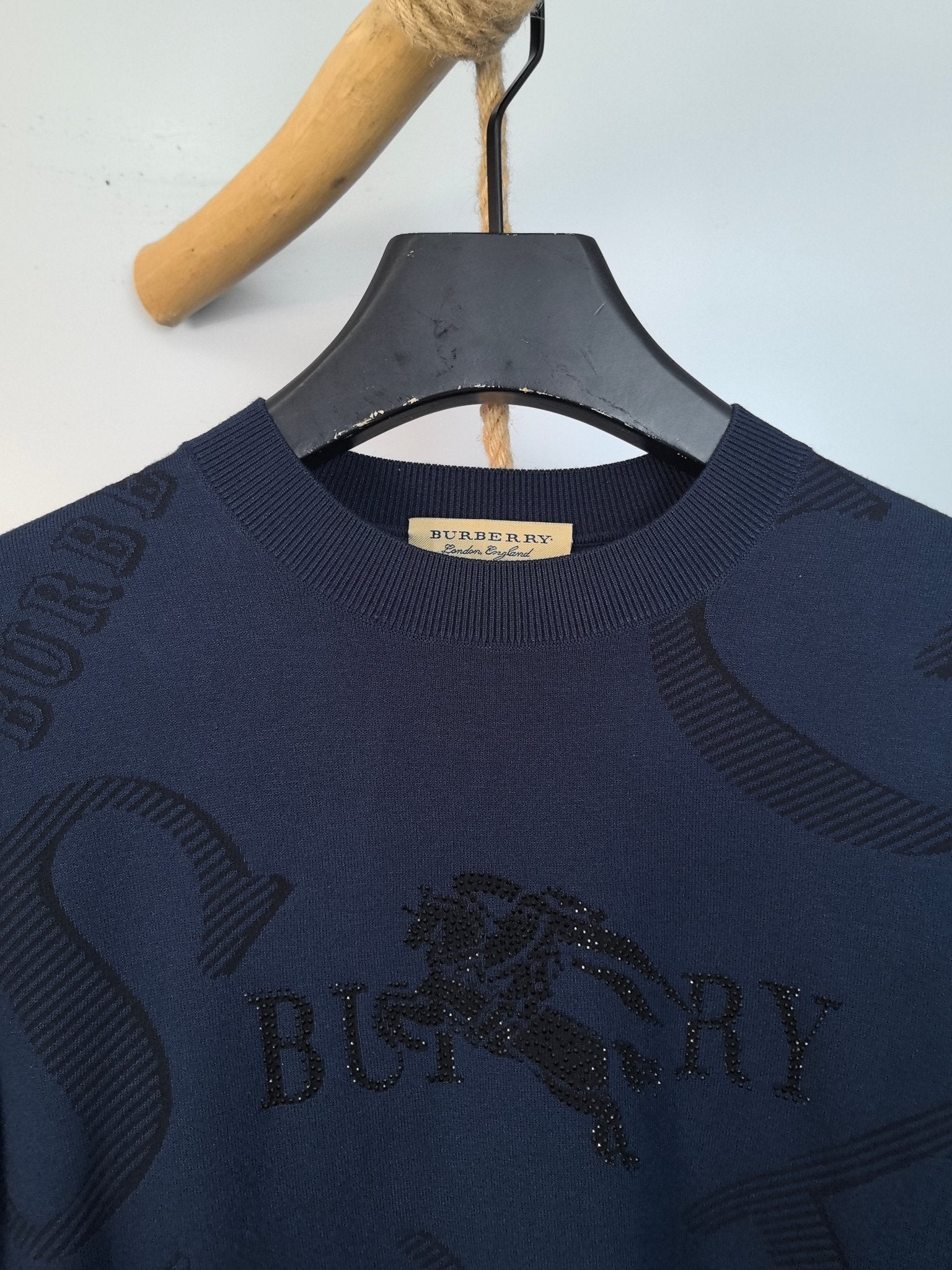 Burberry long-sleeve sweater close-up of crew neck and gold logo patch on collar.