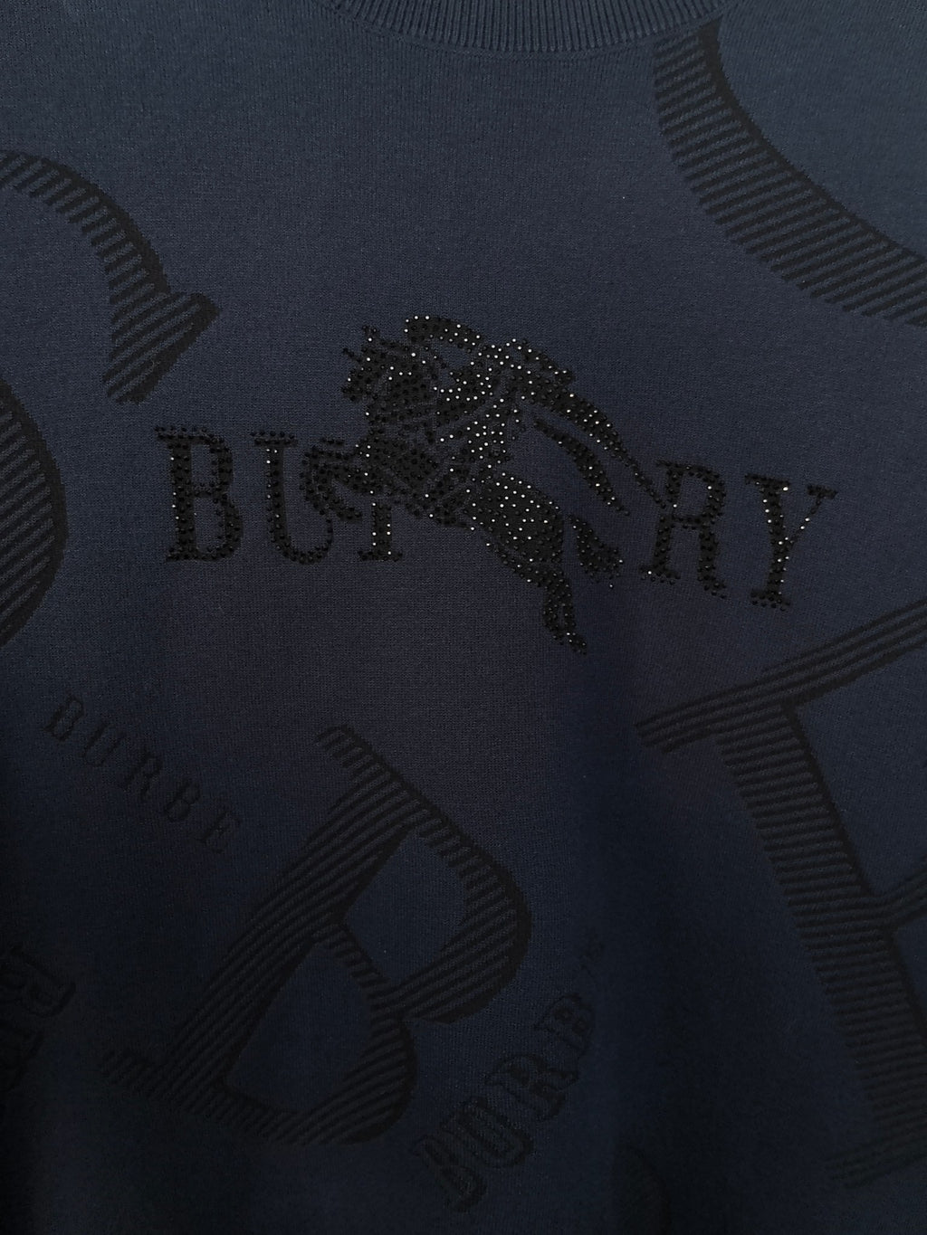 Burberry long-sleeve sweater close-up of dark navy knit with embellished logo detail.