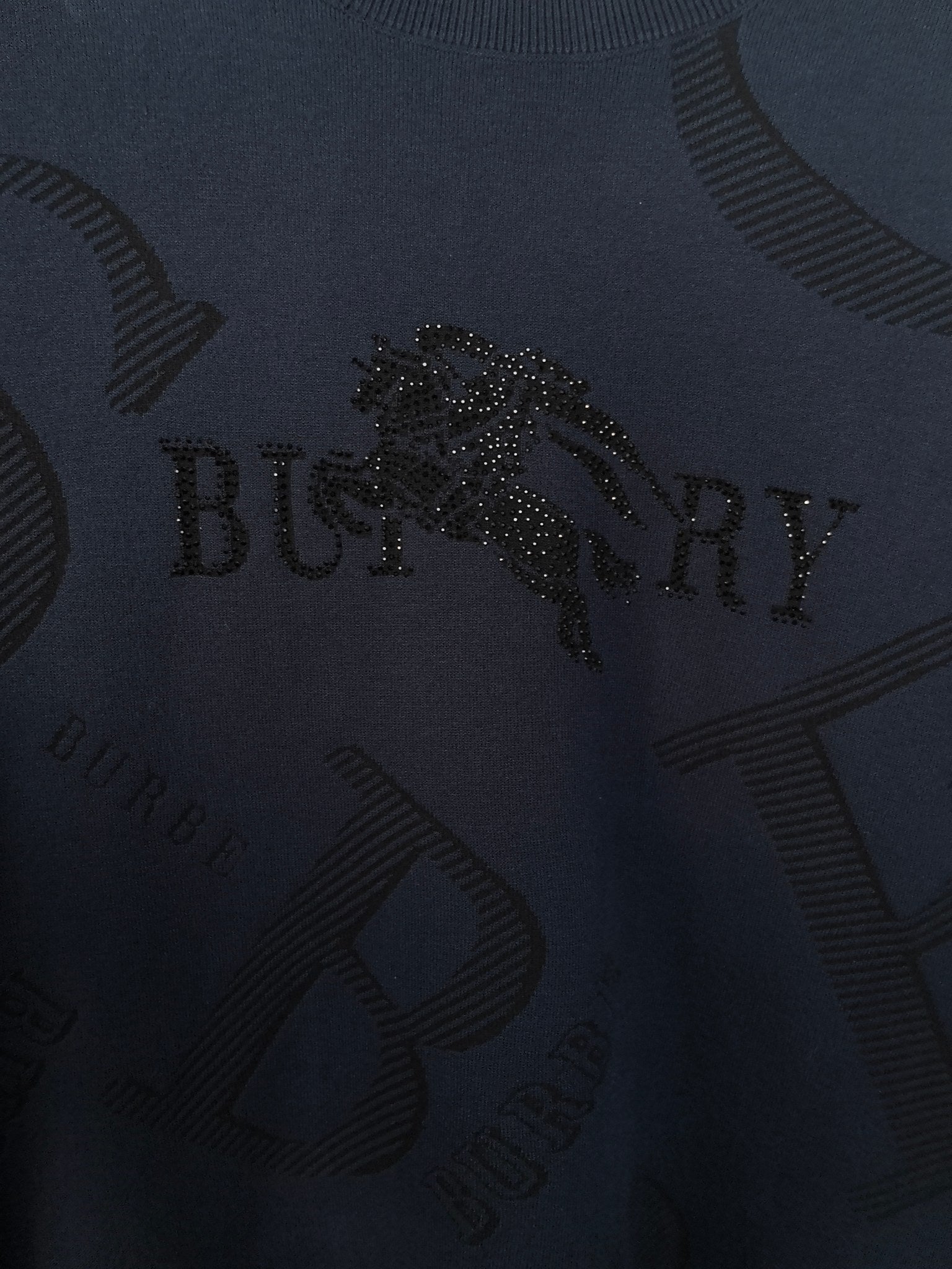 Burberry long-sleeve sweater close-up of dark navy knit with embellished logo detail.