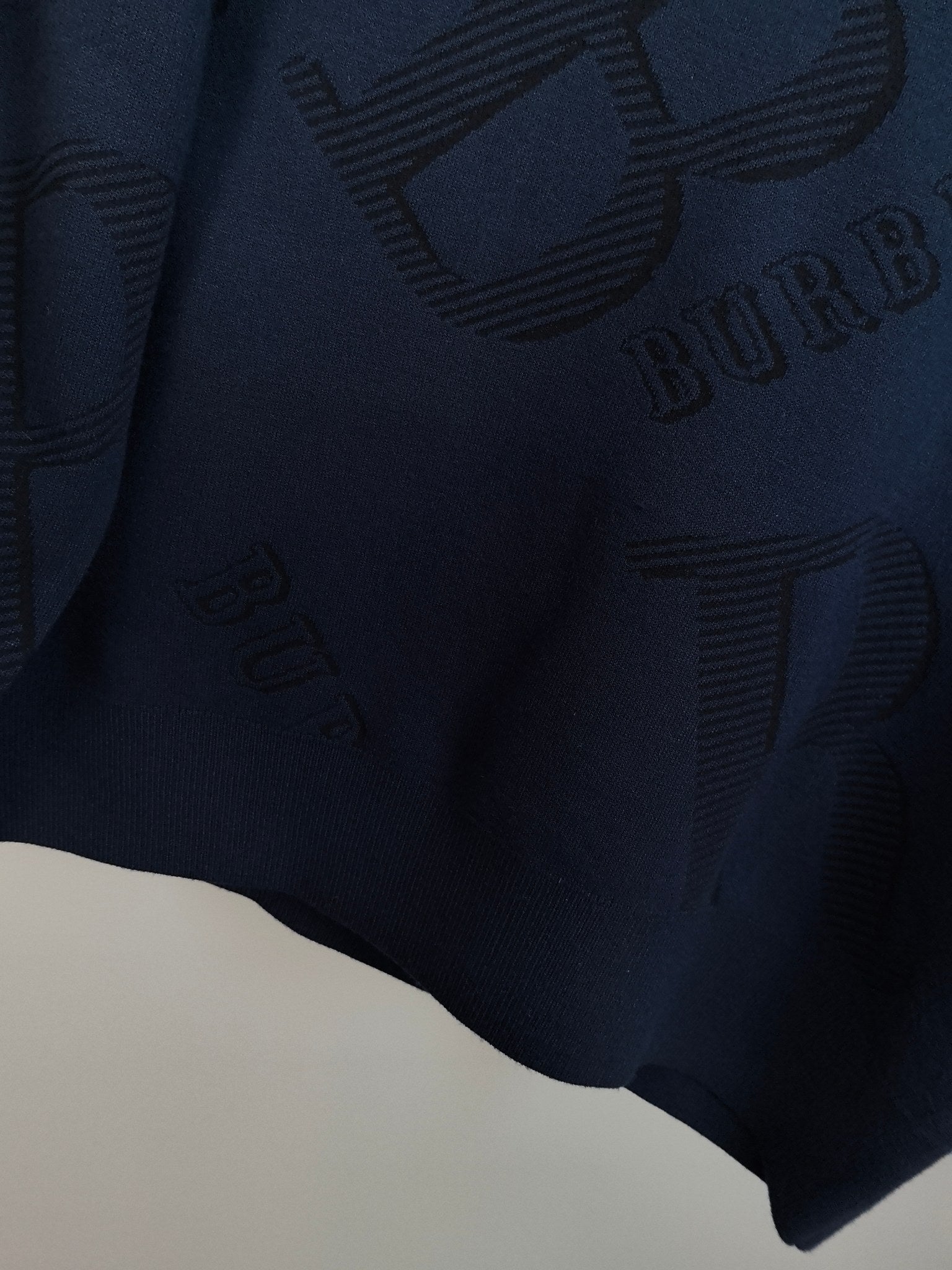 Burberry long-sleeve sweater close-up of allover ribbed logo pattern on fabric.