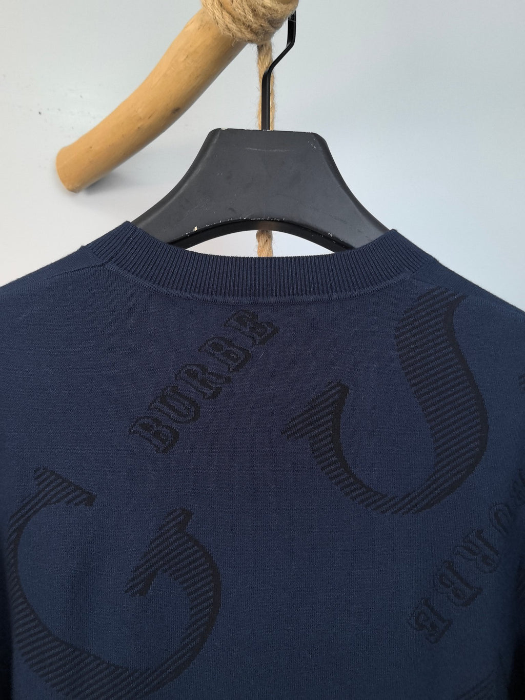 Burberry long-sleeve sweater back close-up with “B” logo and crew neckline.