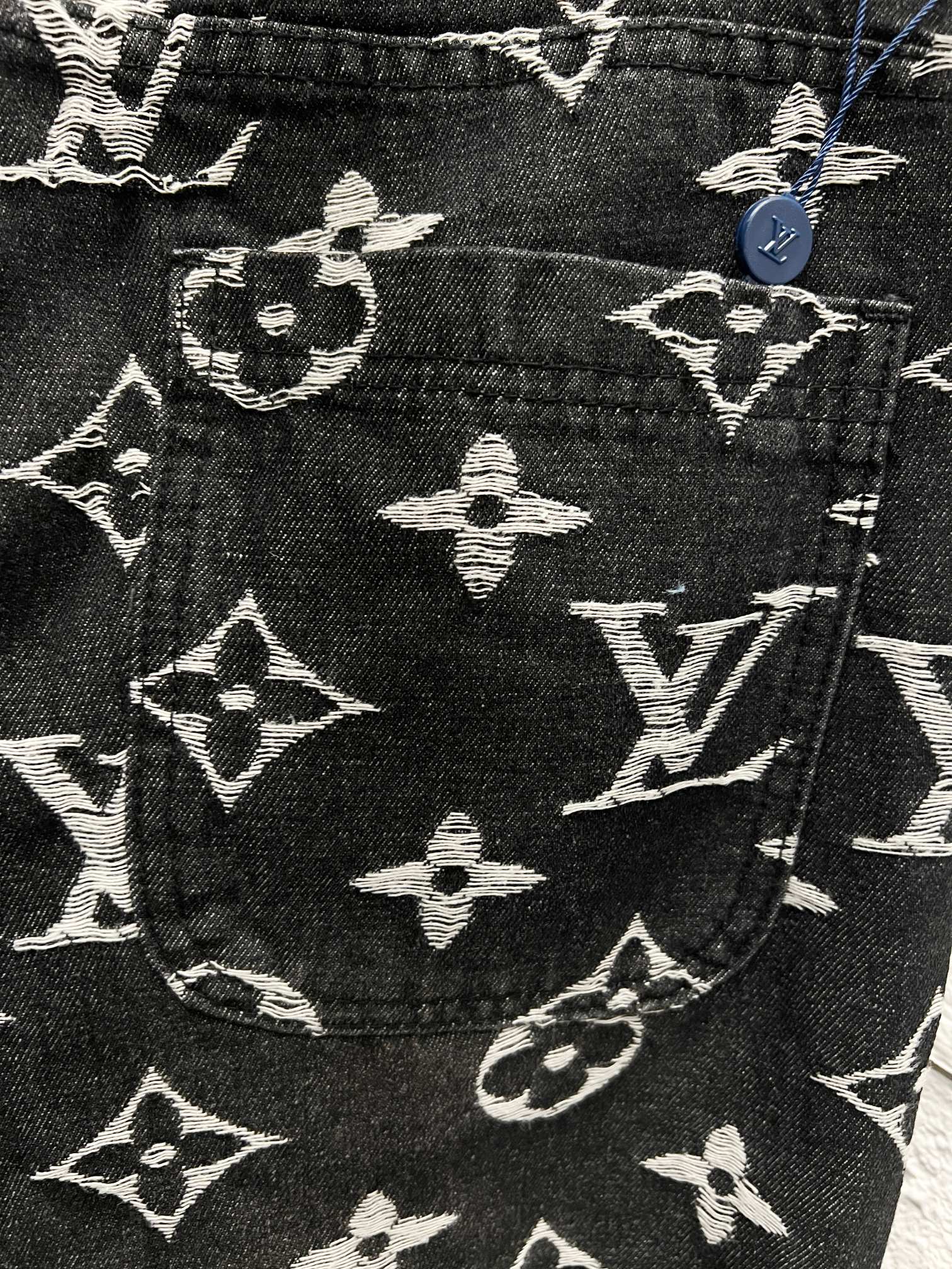 Louis Vuitton monogram print pants front detail, dark fabric with white scattered symbols
