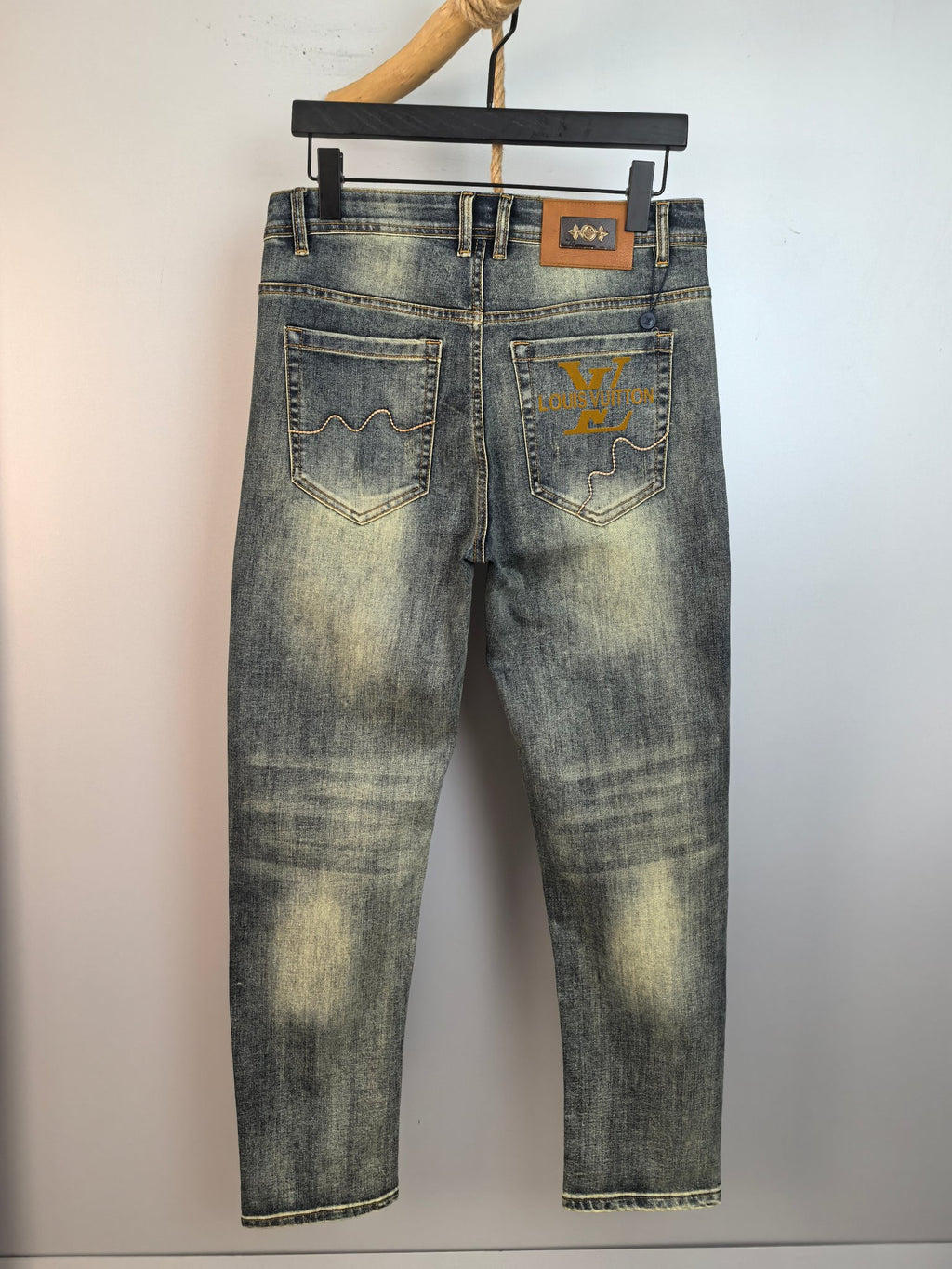Light-wash denim pants with front pockets and small logo patch, hanging view