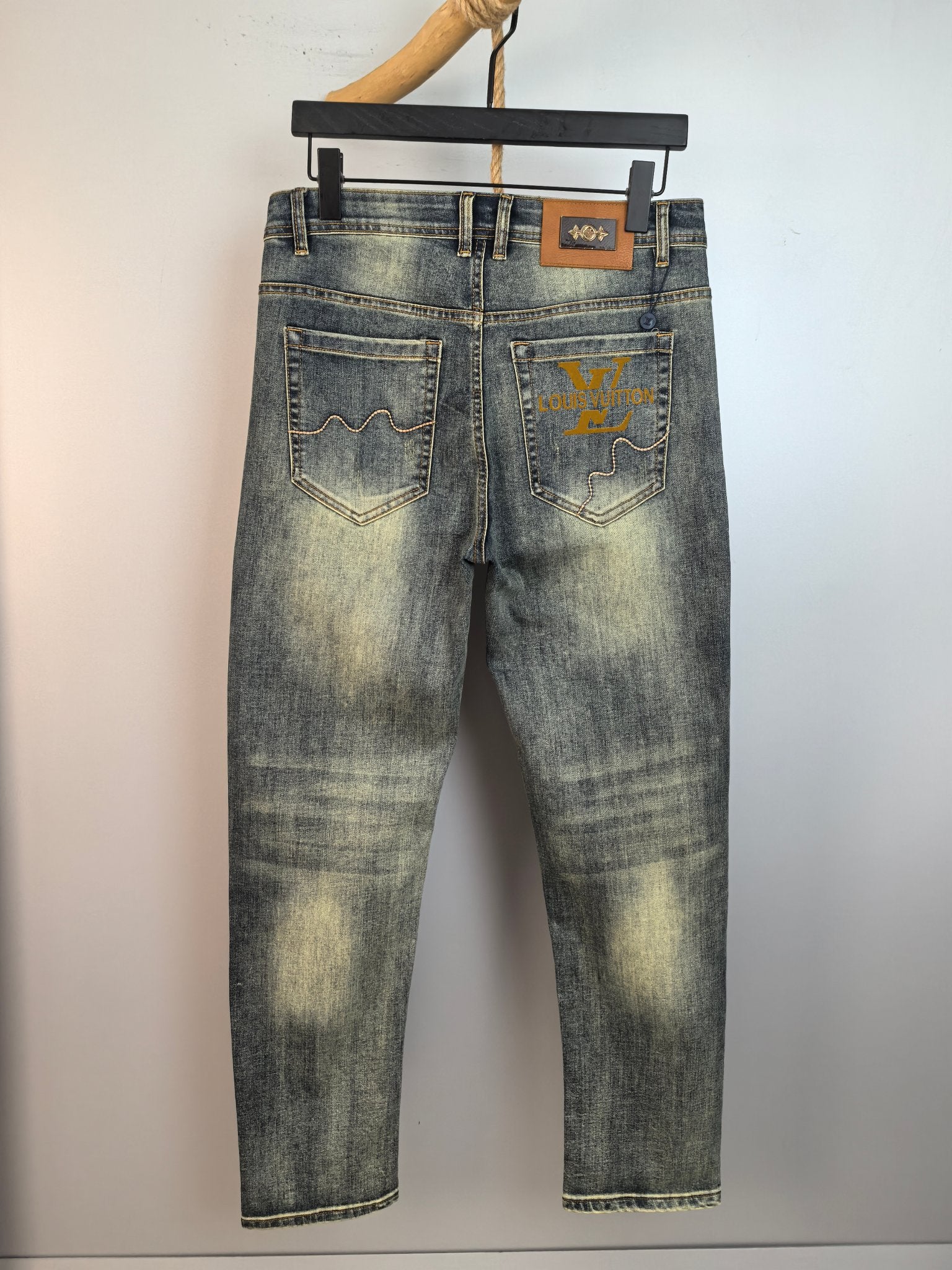 Light-wash denim pants with front pockets and small logo patch, hanging view