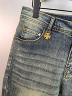 Denim pants with curved pocket stitching and gold-tone charm, angled close-up