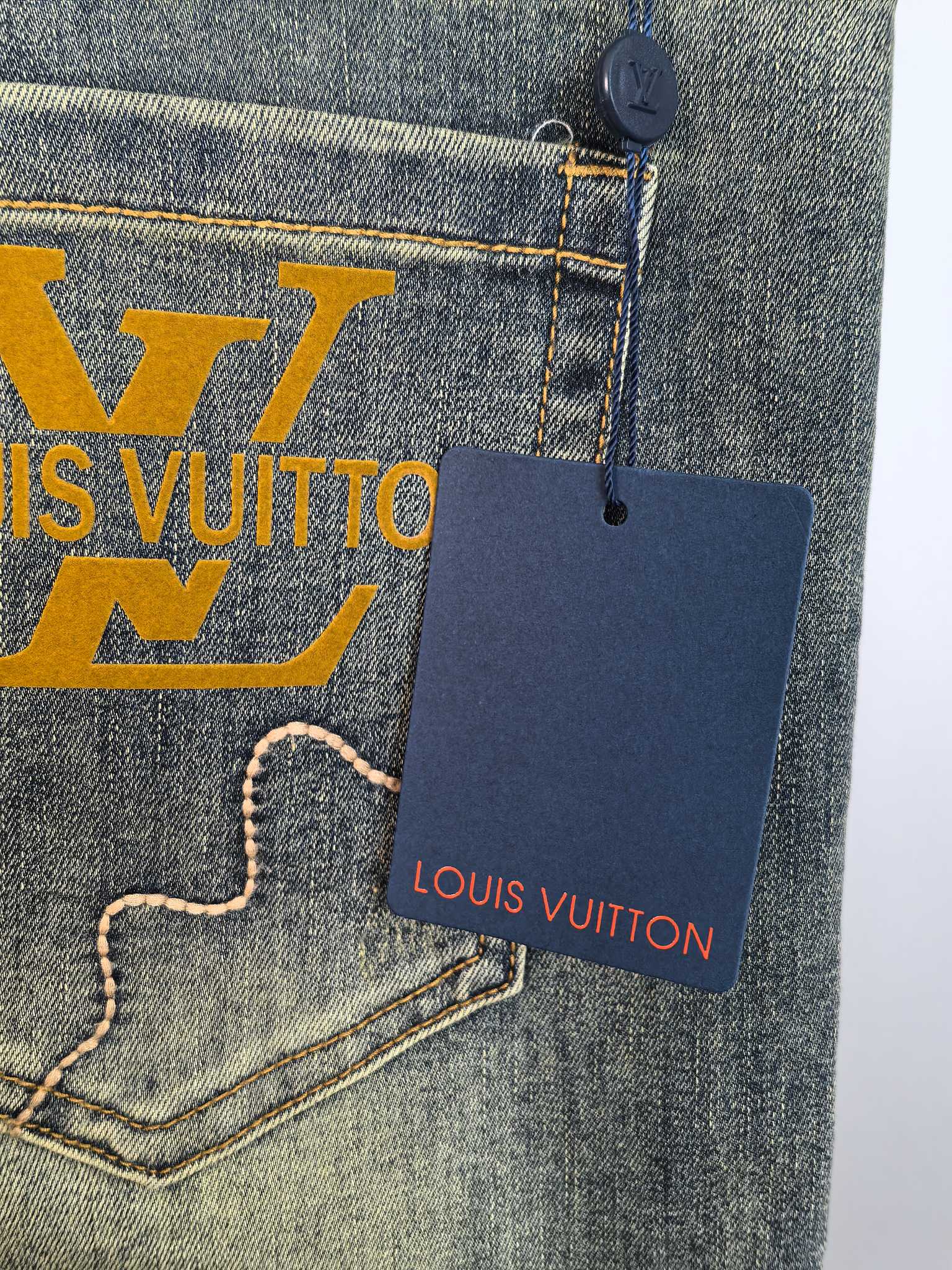 Denim pocket with large LV graphic and hanging Louis Vuitton tag, close-up