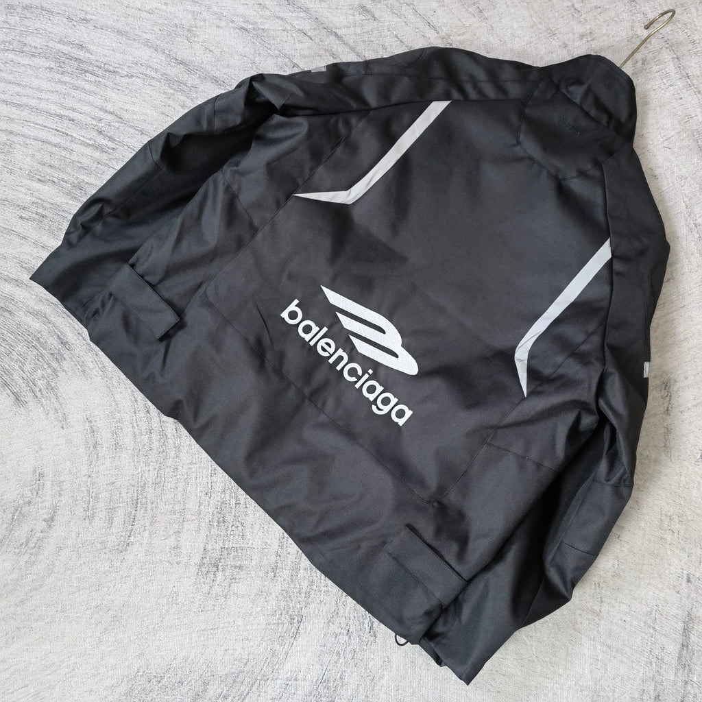 Black zip-up jacket laid flat with white Balenciaga logo and logo stripe on the back