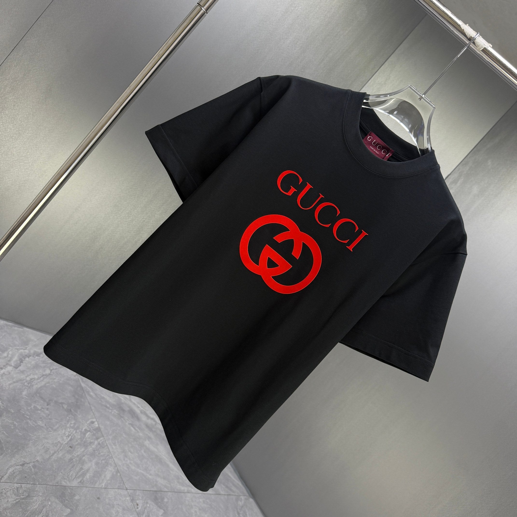 Black Gucci short-sleeve T-shirt with red Gucci logo, shown at an angle on a hanger
