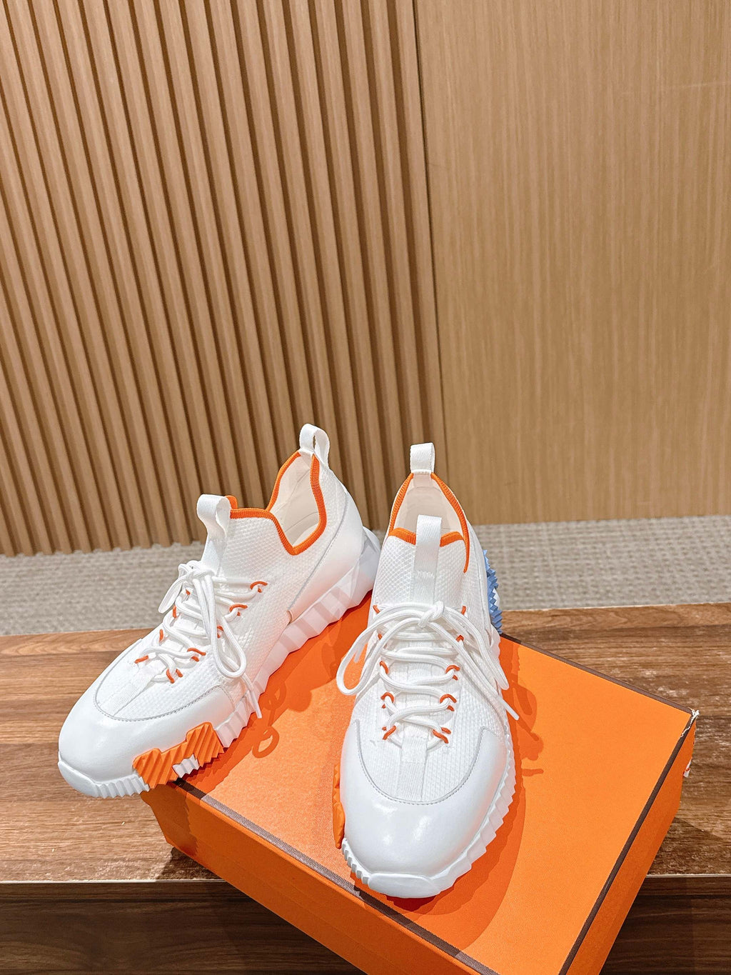 Hermes unisex sneakers, angled view with white uppers and orange-and-blue sole accents.