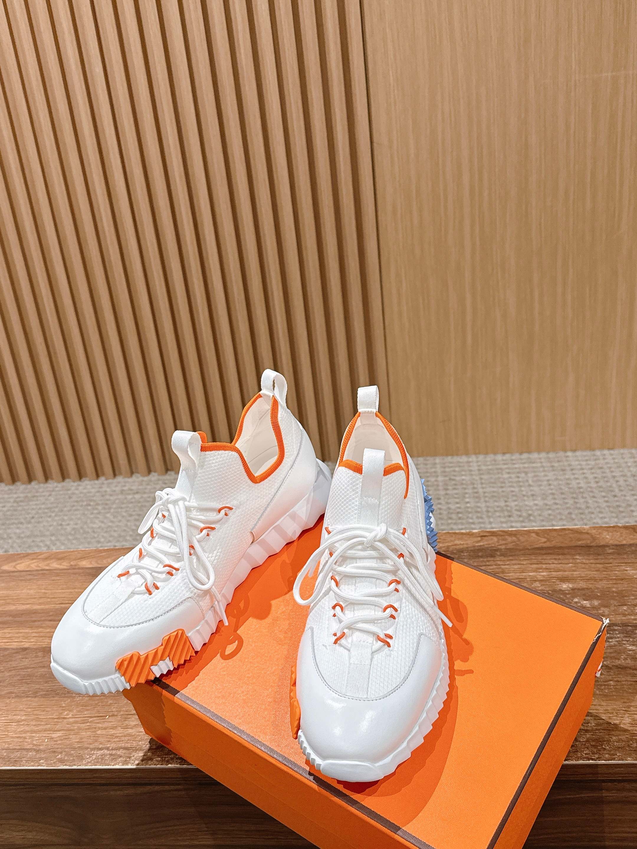 Hermes unisex sneakers, angled view with white uppers and orange-and-blue sole accents.