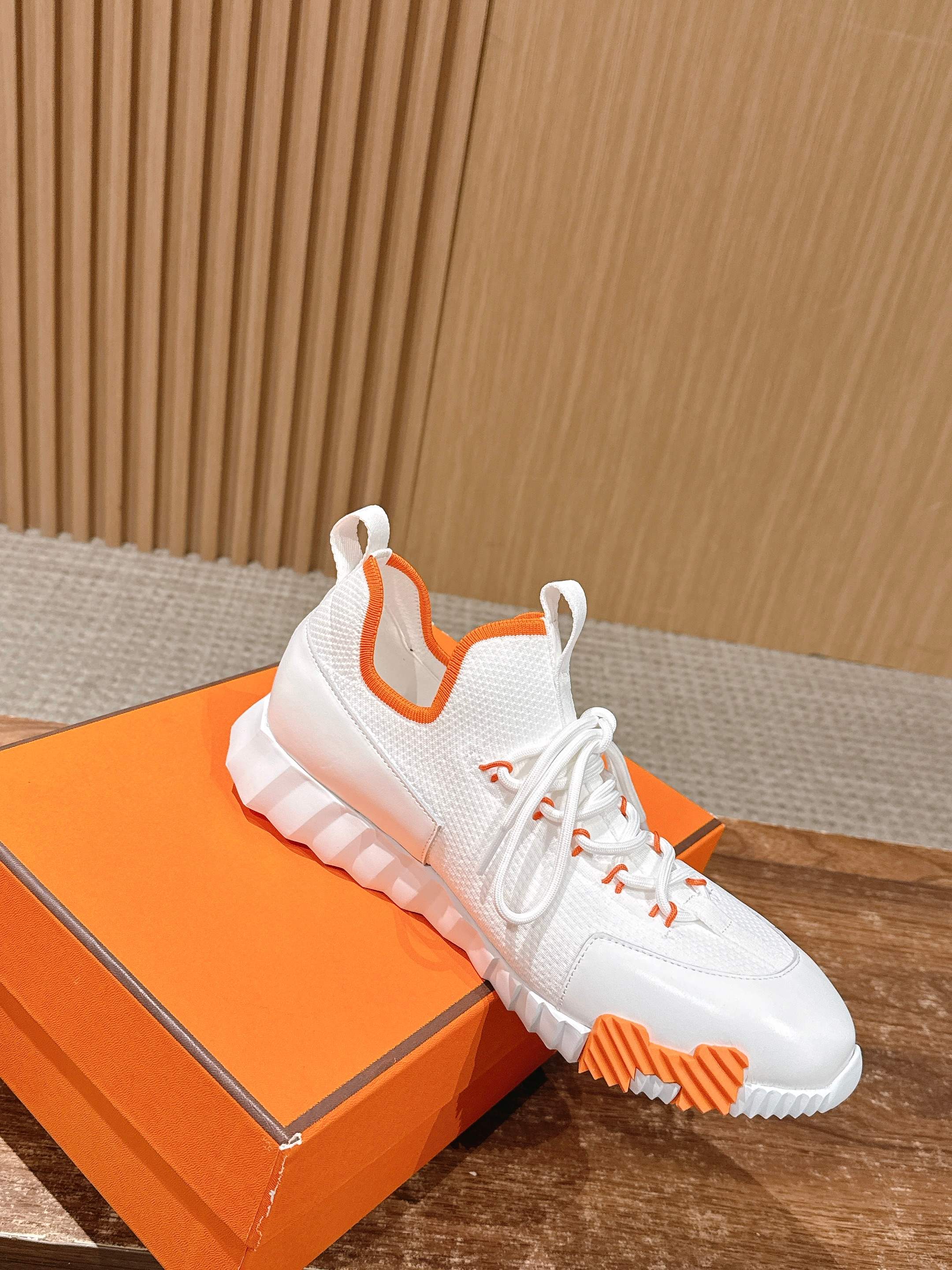 Hermes unisex sneakers on an orange box, white uppers with orange outsole details.