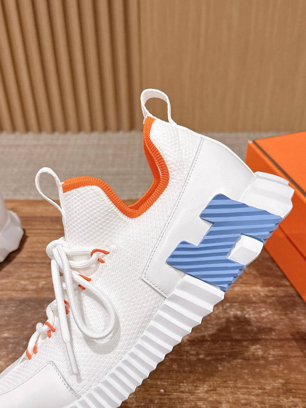 Hermes unisex sneakers close-up: white upper with orange collar and blue logo panel.