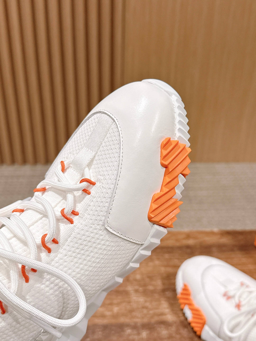 Hermes unisex sneaker close-up: white textured upper with orange heel tab and sole.
