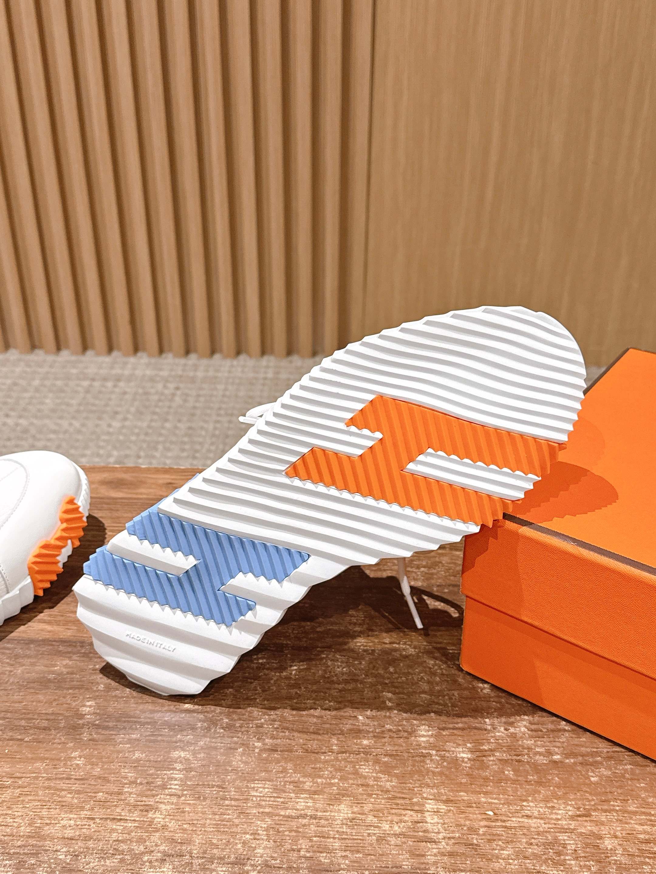 Hermes unisex sneakers outsole close-up, white tread with orange and blue stripe details.
