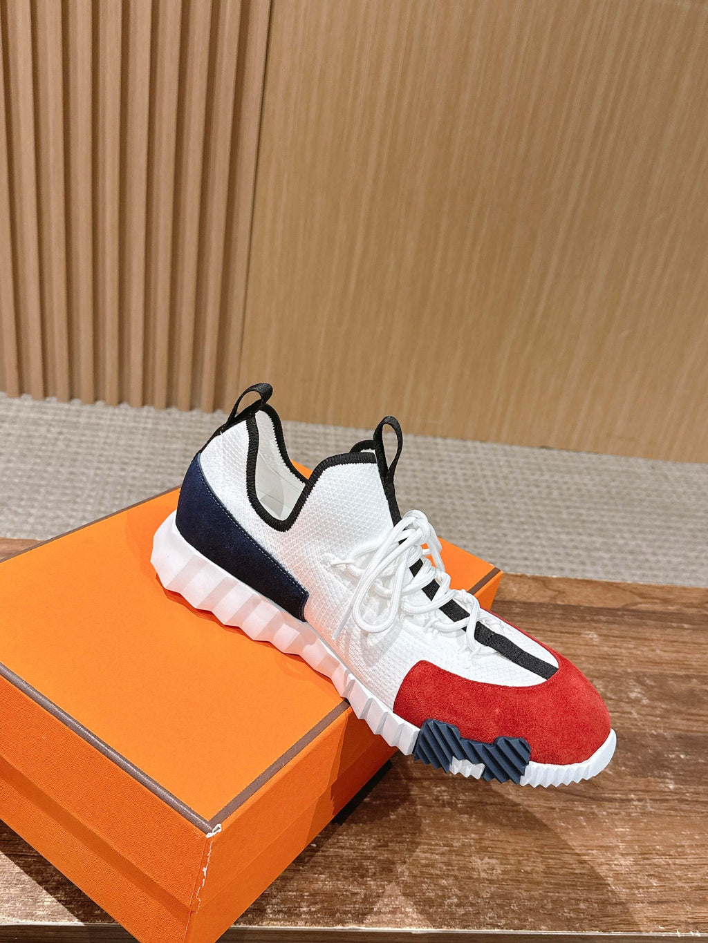 White unisex sneaker on orange box, red toe panel, navy side stripe, grippy sole