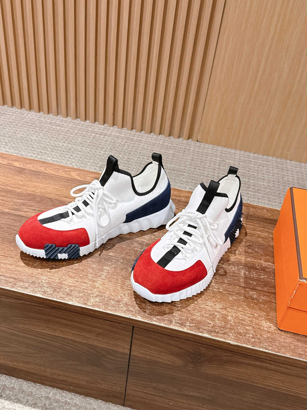 Pair of unisex sneakers, white upper with red and navy accents, black stripes, laced