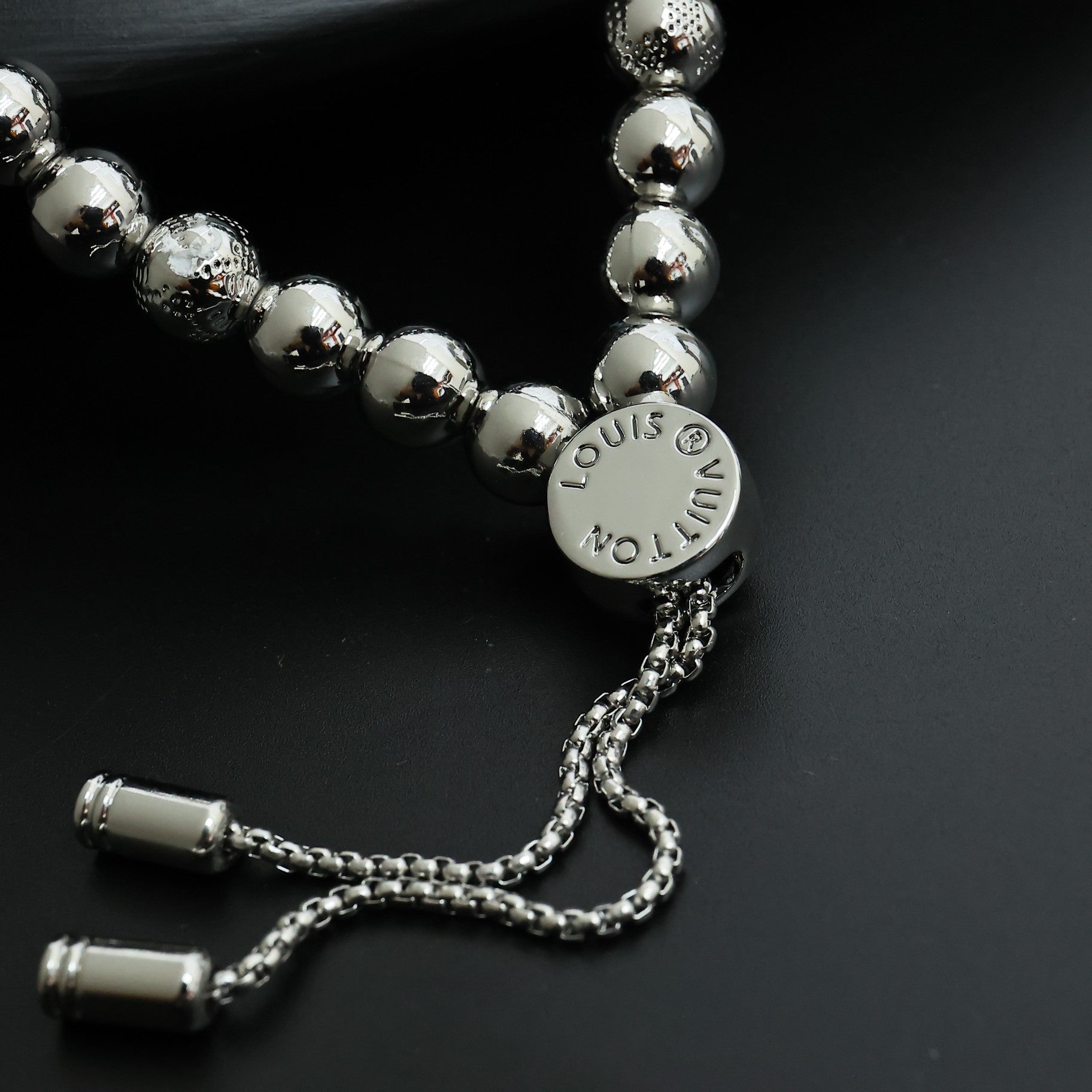 Louis Vuitton beaded bracelet with round silver beads, engraved medallion, and chain tassels