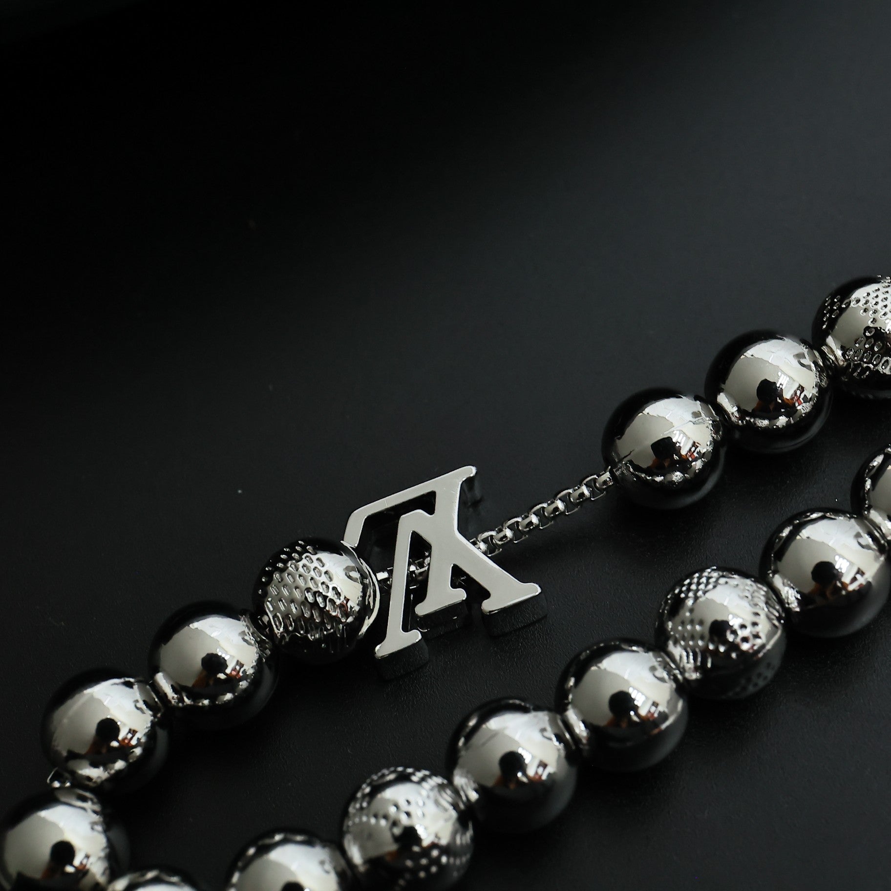 Beaded necklace section with silver-toned beads and LV-style letter charm