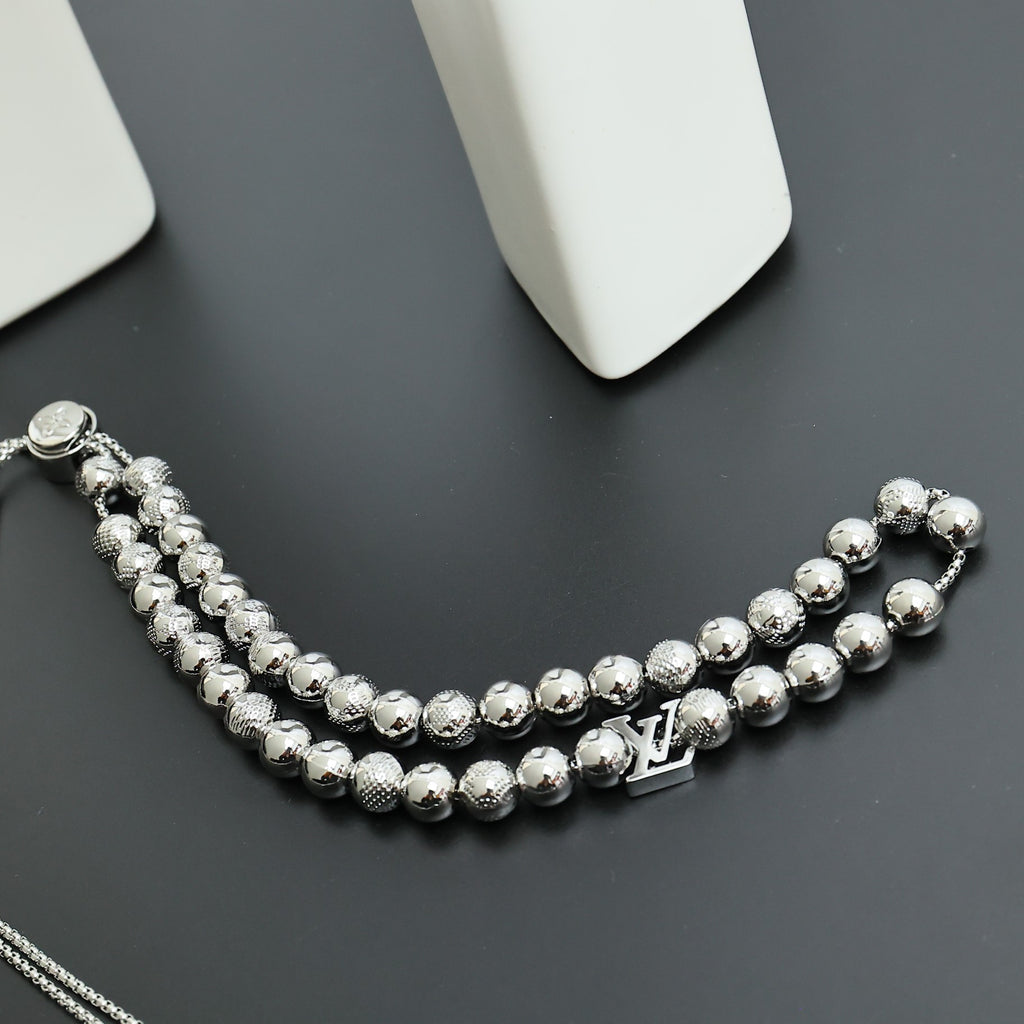 Beaded necklace curved on a dark surface with silver-toned beads and LV charm