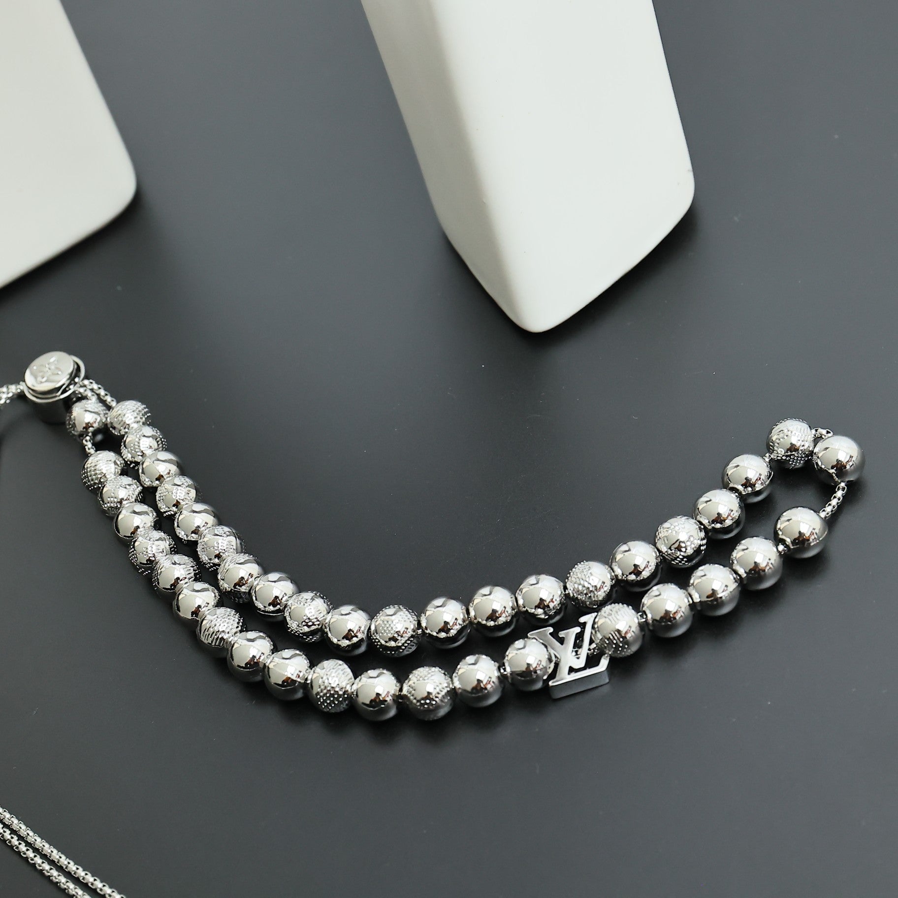 Beaded necklace curved on a dark surface with silver-toned beads and LV charm