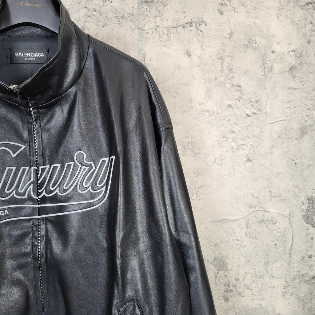 Black leather jacket side close-up with “Luxury” print and partial front zip