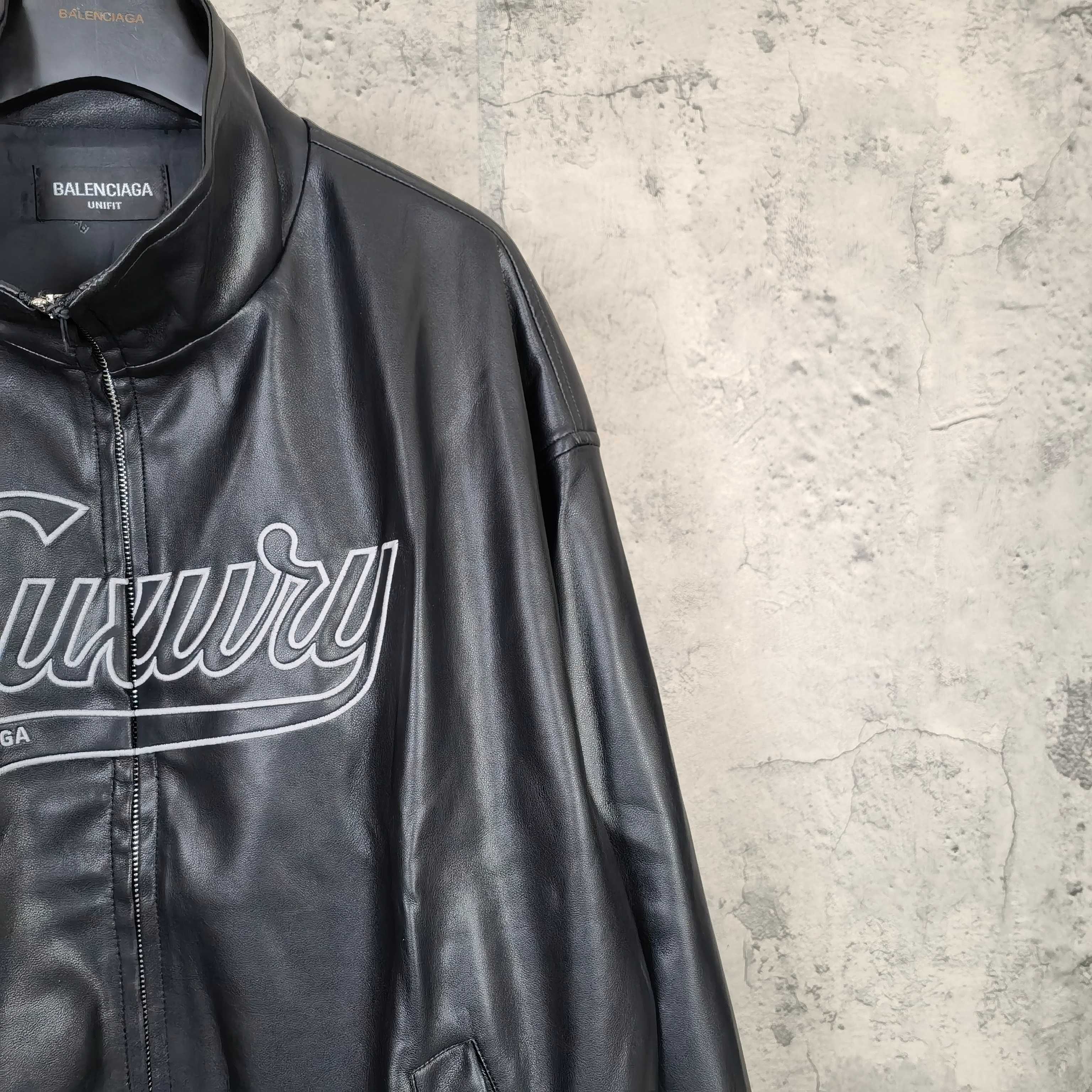 Black leather jacket side close-up with “Luxury” print and partial front zip