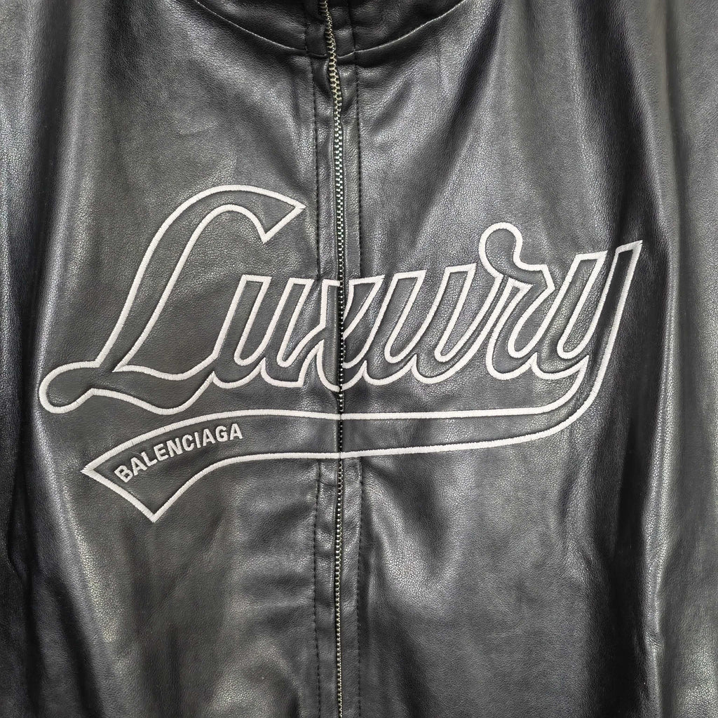 Black leather jacket front close-up of white “Luxury” logo and zip
