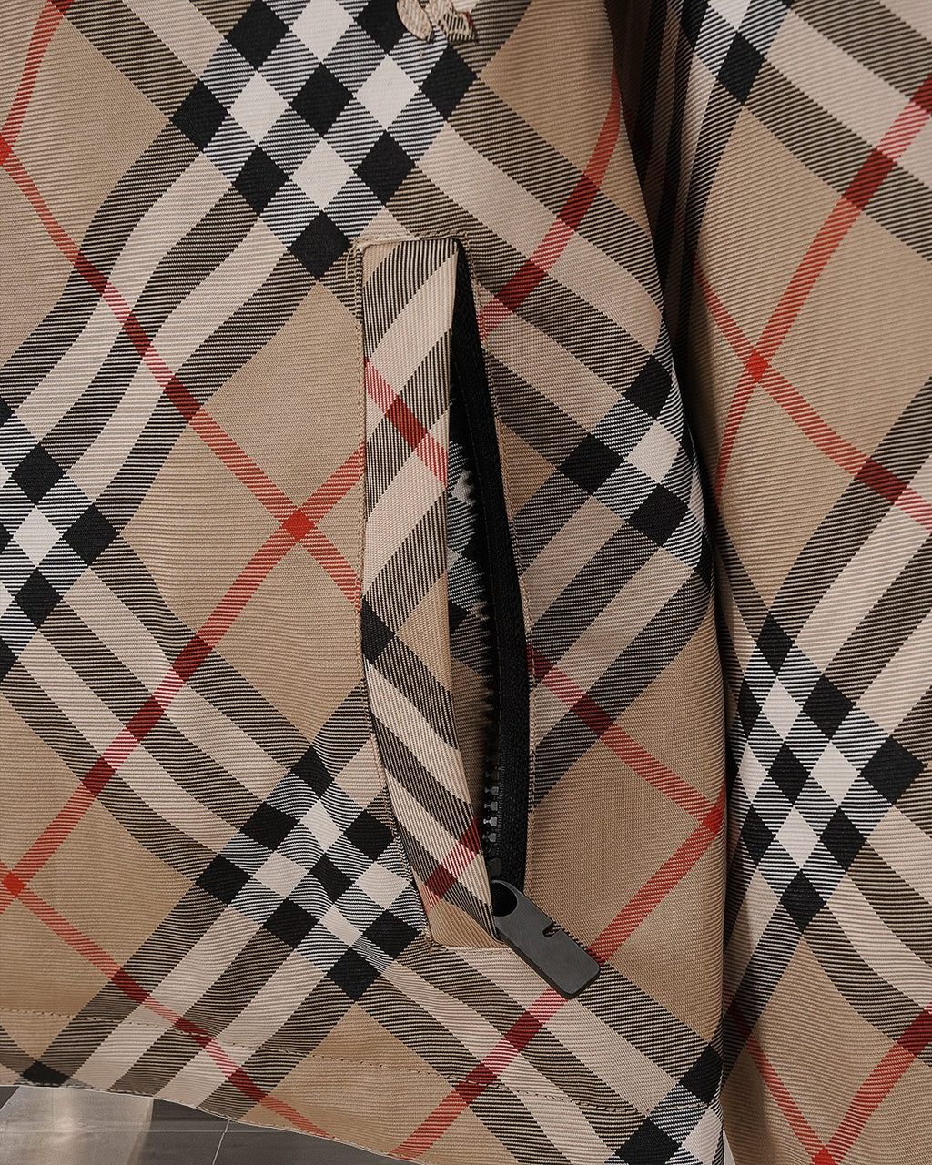 Side seam and zipper guard on beige, black, and red plaid hooded jacket